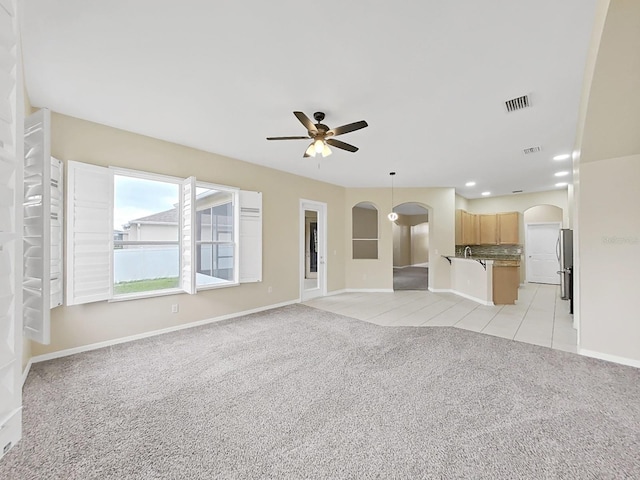 unfurnished living room featuring arched walkways, ceiling fan, light carpet, and visible vents