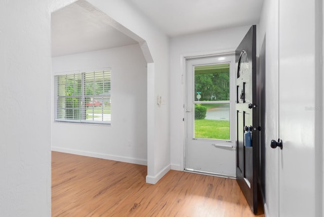 entrance foyer featuring arched walkways, light wood finished floors, a wealth of natural light, and baseboards