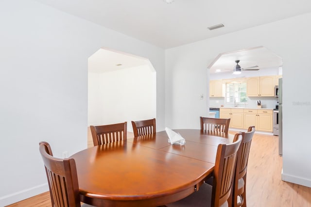 dining area with baseboards, visible vents, arched walkways, ceiling fan, and light wood-style floors