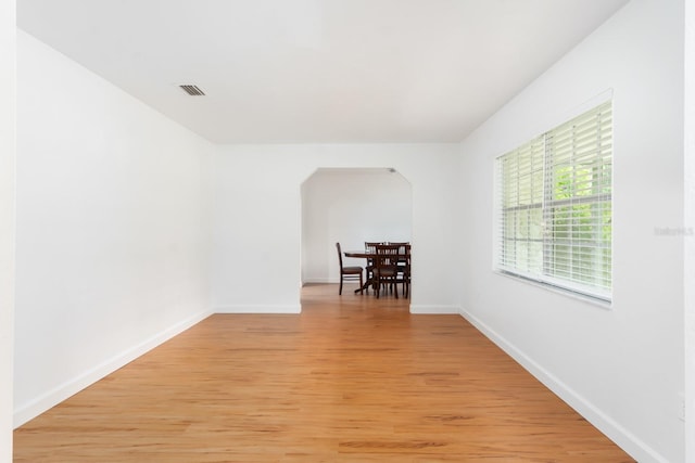 spare room featuring arched walkways, light wood-type flooring, visible vents, and baseboards