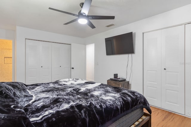 bedroom featuring light wood finished floors, ceiling fan, visible vents, and multiple closets