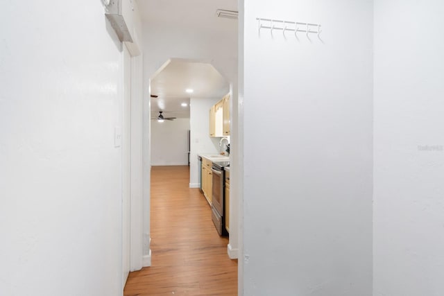 hallway with arched walkways, light wood finished floors, a sink, and baseboards