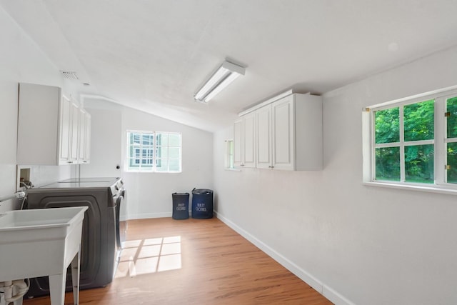 laundry room with light wood-type flooring, independent washer and dryer, cabinet space, and a healthy amount of sunlight