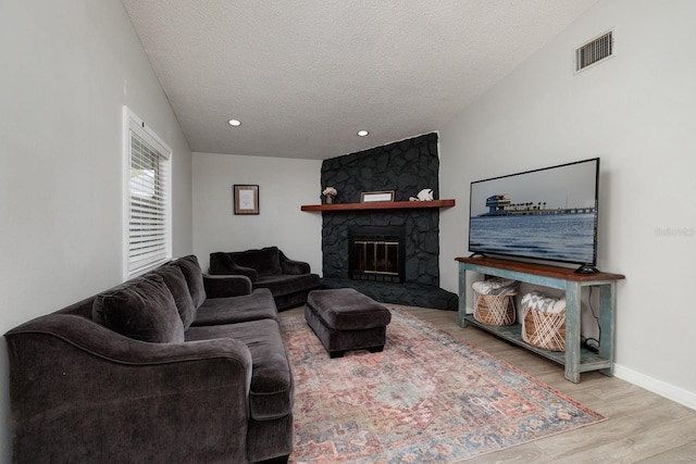 living room with visible vents, a stone fireplace, a textured ceiling, wood finished floors, and baseboards