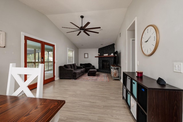 living area featuring a stone fireplace, a ceiling fan, light wood-style floors, vaulted ceiling, and french doors