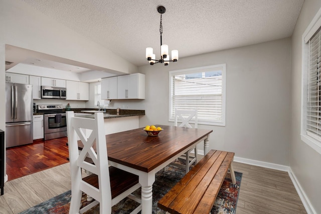 dining space with dark wood finished floors, lofted ceiling, a textured ceiling, a chandelier, and baseboards