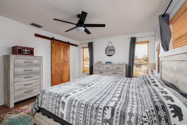 bedroom with a barn door, visible vents, dark wood-style floors, ceiling fan, and a textured ceiling