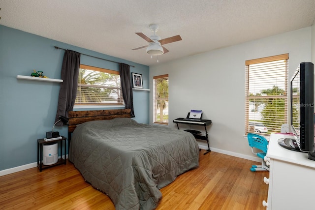 bedroom featuring light wood-style floors, a ceiling fan, baseboards, and a textured ceiling