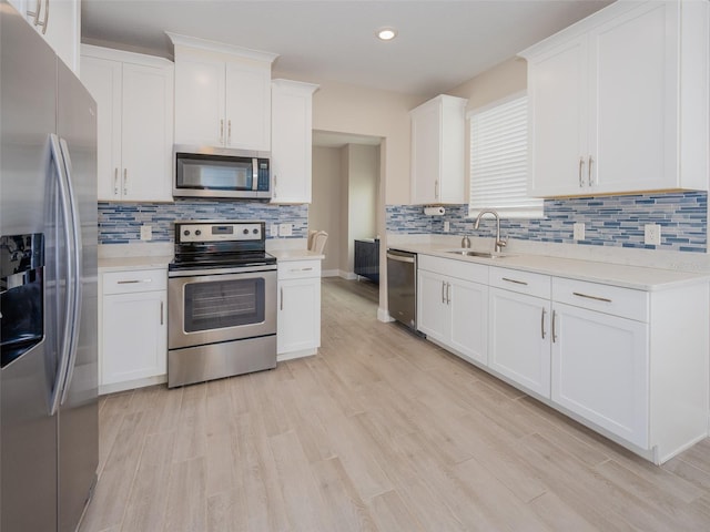 kitchen with light wood-style flooring, a sink, white cabinets, light countertops, and appliances with stainless steel finishes