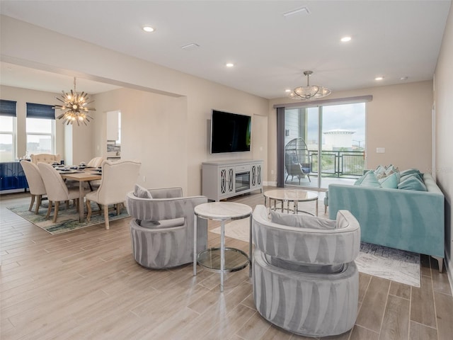 living area with wood tiled floor, a healthy amount of sunlight, recessed lighting, and an inviting chandelier