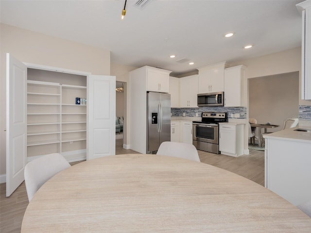 kitchen with tasteful backsplash, light countertops, appliances with stainless steel finishes, light wood-style floors, and white cabinets