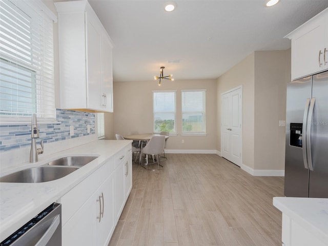 kitchen featuring light wood finished floors, decorative backsplash, appliances with stainless steel finishes, white cabinetry, and a sink