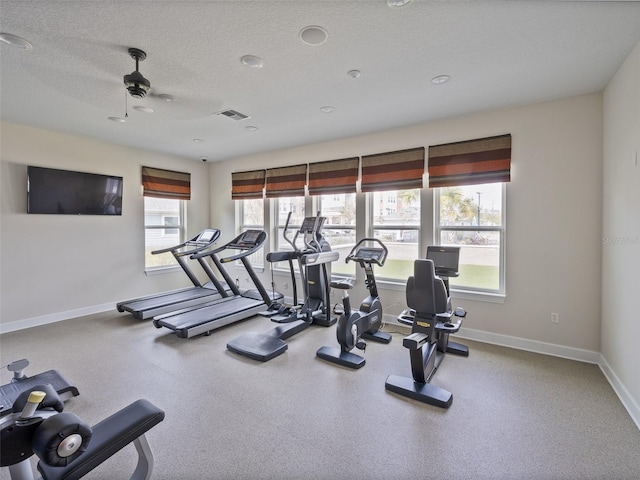 workout area featuring a textured ceiling, ceiling fan, visible vents, and baseboards