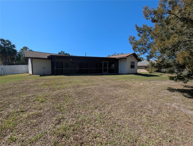 rear view of house featuring a lawn, fence, and a sunroom