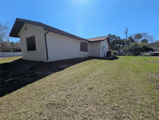 view of side of home with stucco siding, fence, and a yard