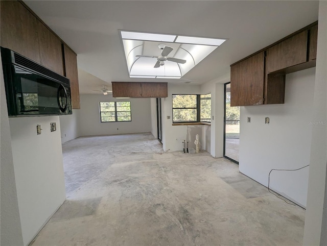 kitchen featuring black microwave, ceiling fan, dark brown cabinetry, unfinished concrete flooring, and a raised ceiling