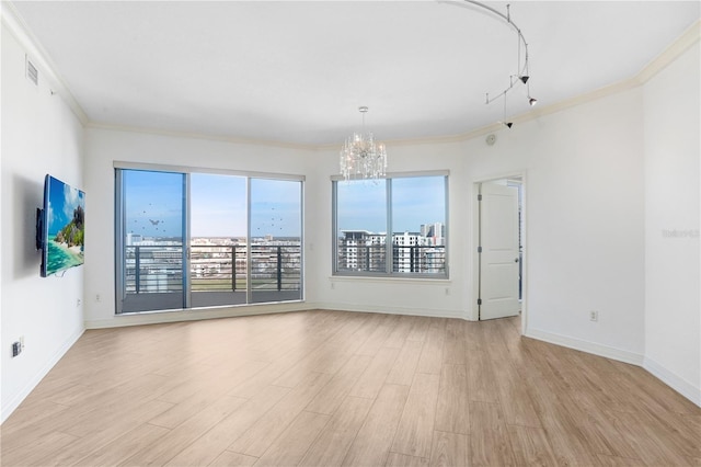 unfurnished room with light wood-type flooring, an inviting chandelier, baseboards, and crown molding