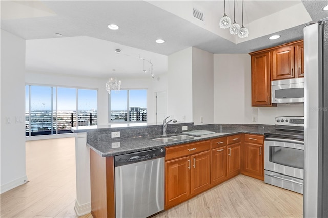 kitchen featuring appliances with stainless steel finishes, brown cabinetry, a sink, and a peninsula