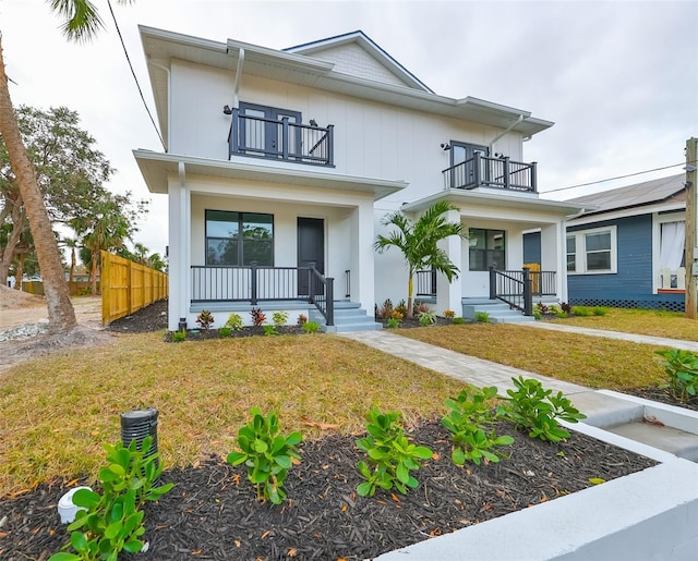 view of front of property featuring a porch, a balcony, fence, board and batten siding, and a front yard