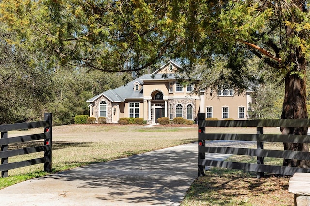 french country home with stone siding, a front lawn, fence, and stucco siding