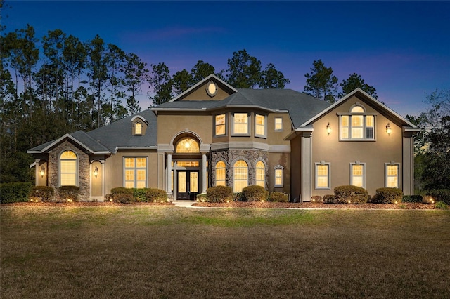 french country style house with stone siding, french doors, a lawn, and stucco siding