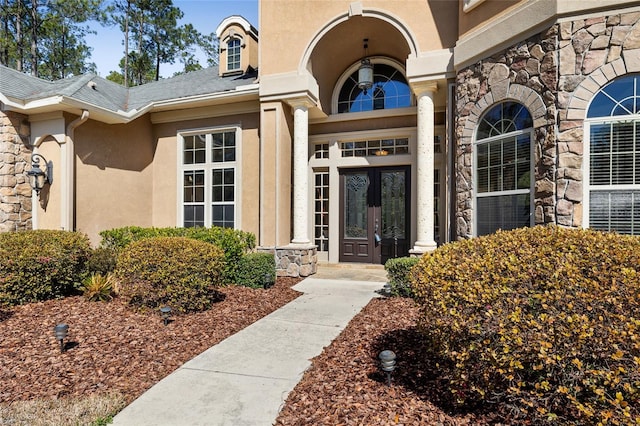 view of exterior entry featuring stone siding, french doors, and stucco siding