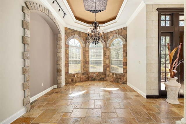 unfurnished dining area with baseboards, ornamental molding, a raised ceiling, and stone tile floors