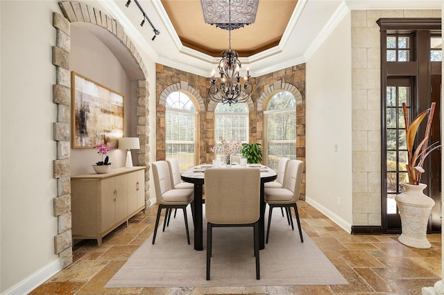 dining area featuring a notable chandelier, stone tile floors, baseboards, ornamental molding, and a raised ceiling