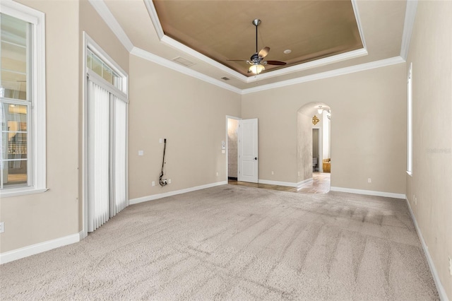 empty room with arched walkways, a raised ceiling, a ceiling fan, ornamental molding, and carpet floors