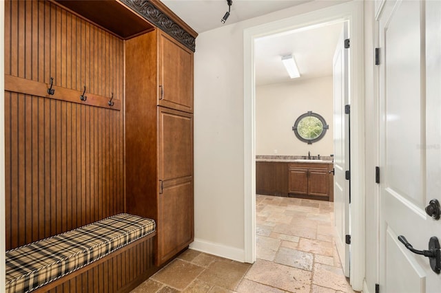 mudroom featuring baseboards, a sink, and stone tile floors