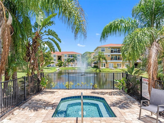 view of pool featuring a community hot tub, a water view, fence, and a residential view