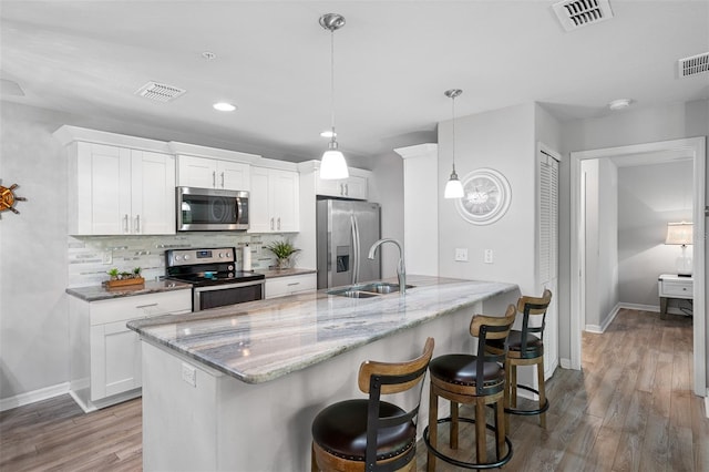 kitchen with appliances with stainless steel finishes, visible vents, decorative backsplash, and wood finished floors