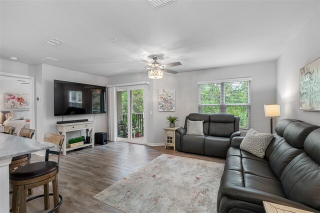 living room with baseboards, wood finished floors, visible vents, and a ceiling fan