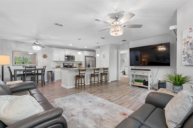 living room featuring ceiling fan, light wood-type flooring, and visible vents