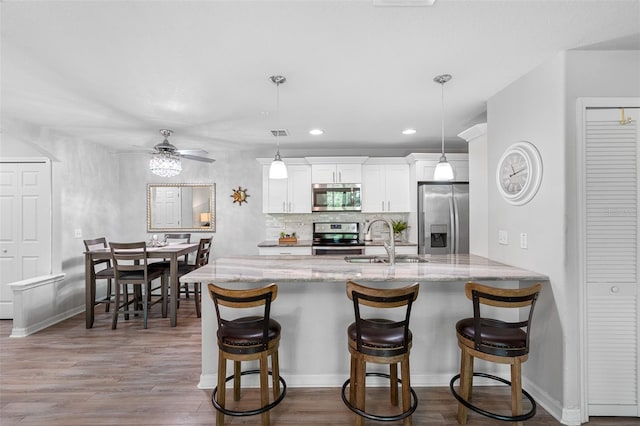 kitchen featuring appliances with stainless steel finishes, dark wood-type flooring, a kitchen bar, white cabinetry, and a sink