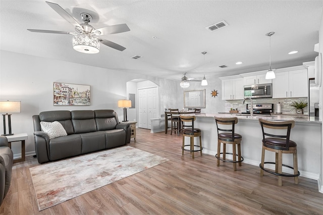 living area with arched walkways, visible vents, ceiling fan, wood finished floors, and baseboards