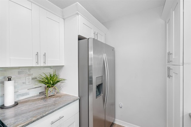 kitchen with stainless steel fridge with ice dispenser, decorative backsplash, white cabinetry, light stone countertops, and baseboards