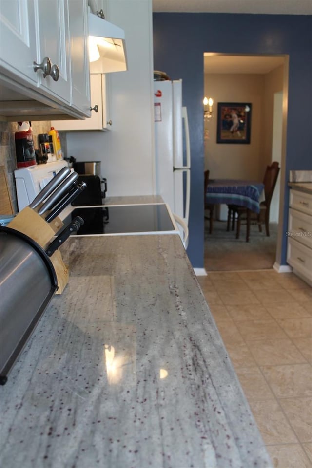 kitchen featuring freestanding refrigerator, light tile patterned flooring, white cabinets, light stone countertops, and under cabinet range hood