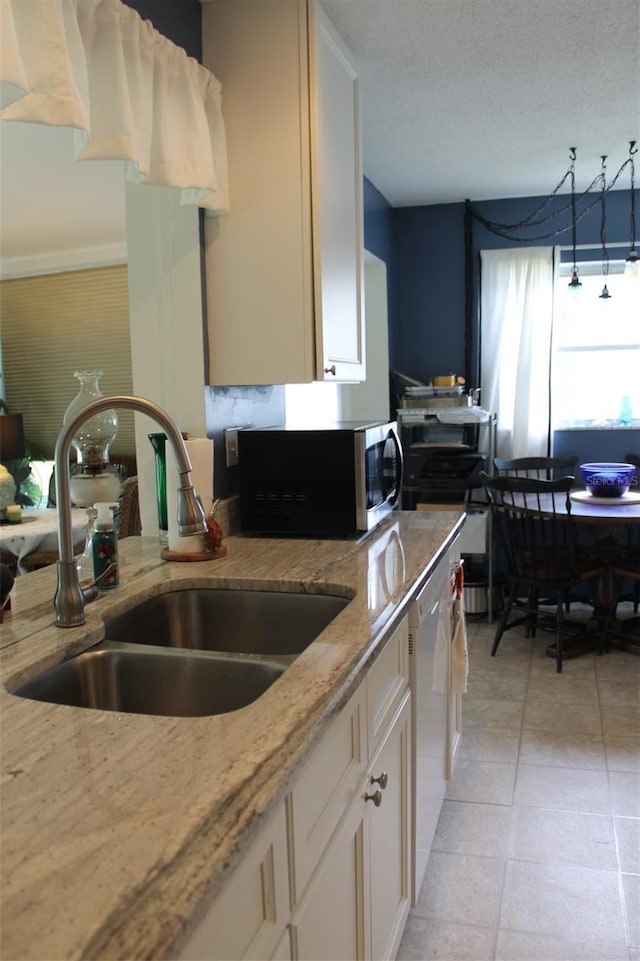 kitchen with light tile patterned floors, light stone counters, white dishwasher, a sink, and stainless steel microwave