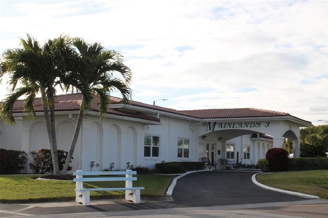 view of front of property featuring driveway, a front yard, a tiled roof, and stucco siding