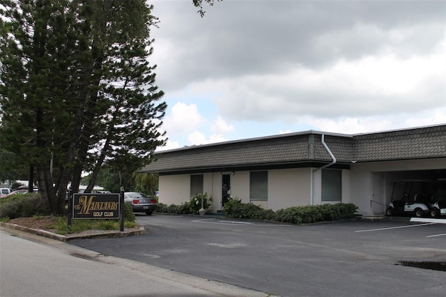 exterior space with uncovered parking, mansard roof, and stucco siding