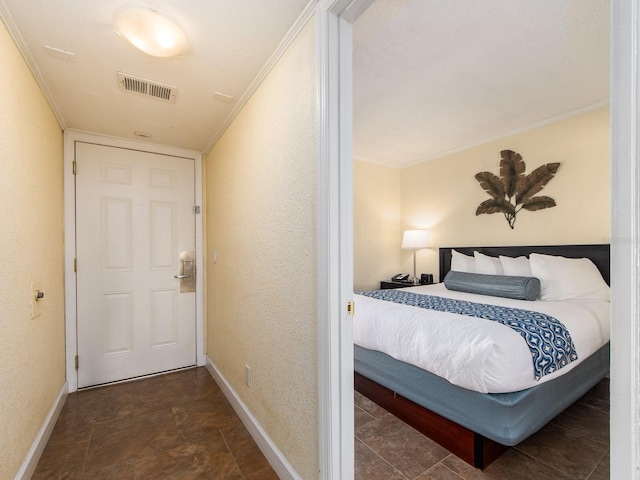 bedroom with a textured wall, ornamental molding, visible vents, and baseboards