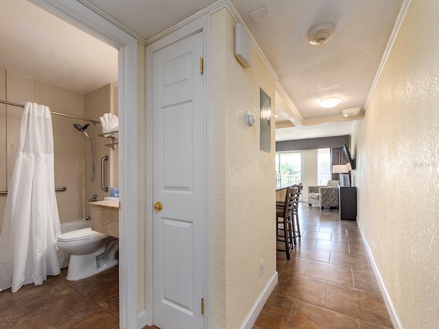 corridor featuring baseboards, a textured wall, a textured ceiling, and crown molding