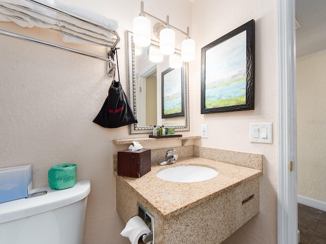 half bathroom featuring a textured wall, vanity, and toilet