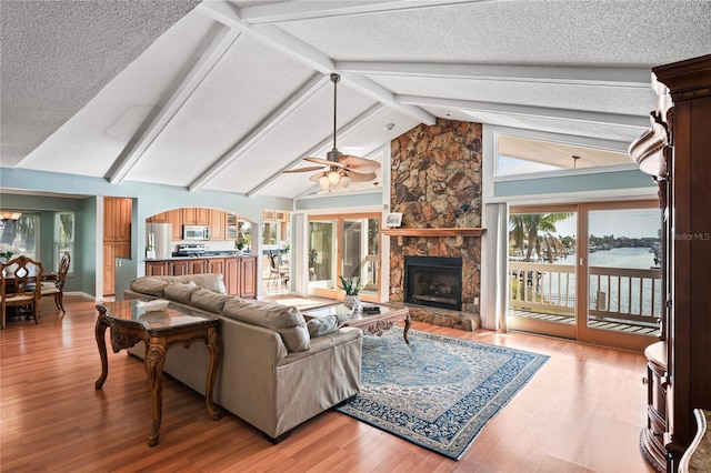 living room featuring a fireplace, light wood finished floors, a textured ceiling, high vaulted ceiling, and beamed ceiling