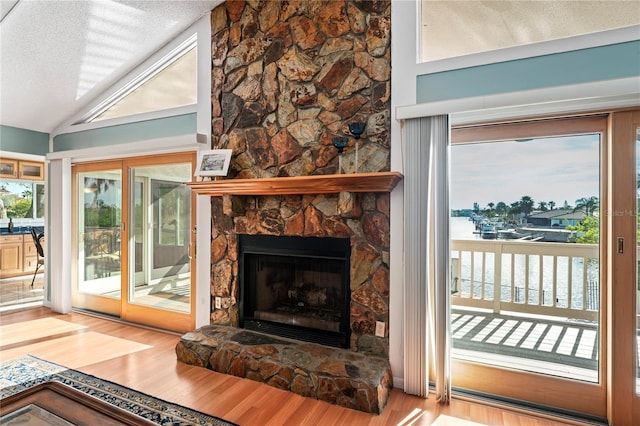 living room featuring a textured ceiling, a stone fireplace, vaulted ceiling, and wood finished floors