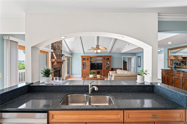 kitchen featuring arched walkways, open floor plan, a sink, a stone fireplace, and stainless steel dishwasher