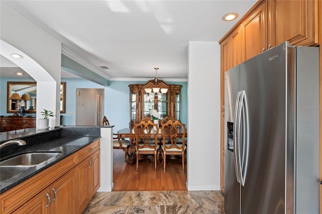 kitchen featuring a notable chandelier, stainless steel refrigerator with ice dispenser, brown cabinetry, dark stone countertops, and crown molding