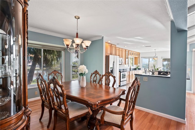 dining area featuring light wood finished floors, crown molding, baseboards, and a notable chandelier