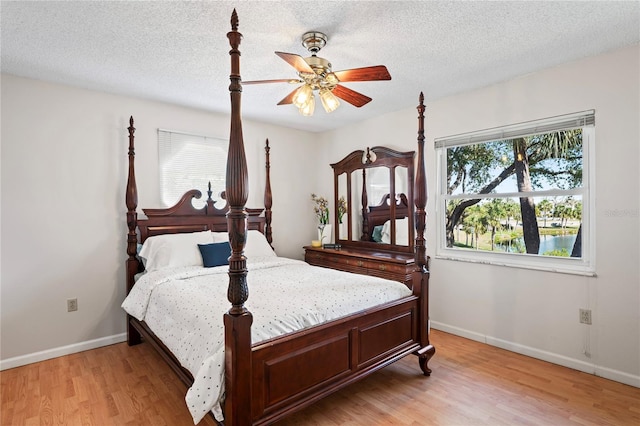 bedroom featuring a textured ceiling, light wood-type flooring, a ceiling fan, and baseboards